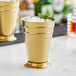 A gold Barfly Deluxe Mint Julep cup with ice and mint leaves on a counter.