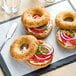 A Schar gluten-free everything bagel with cream cheese, onions, tomato, and cucumber on a black tray.