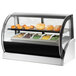 A Vollrath curved glass heated countertop display case with bread and pastries inside.