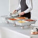 A person in an apron serving food from a Choice disposable chafer dish kit on a table.
