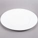An Arcoroc white porcelain service plate with a white rim on a gray surface.