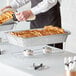 A person pouring food into a Choice disposable chafer dish on a table in a hotel buffet.
