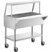 A stainless steel ServIt ice-cooled food table with an angled sneeze guard over three pans on wheels.