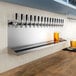 A Regency stainless steel wall mount beer drip tray with 16 faucets above a row of beer taps.