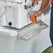 A man using a Regency stainless steel underbar mount beer drip tray to pour a beer into a plastic cup.