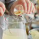 A person pouring Malt Products Organic Agave Syrup into a glass pitcher with lime slices.