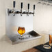 A glass of beer sits on a Regency stainless steel shelf under a beer tap.