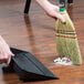 A person using a Heavy-Duty Authentic Amish-Made Corn Whisk Broom to sweep a wood floor.