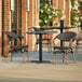 A Lancaster Table & Seating Paladina table with black French bistro chairs on an outdoor patio.