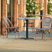 A Lancaster Table & Seating Versilla table with 2 French bistro chairs on a patio.