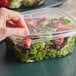 A hand holding a Dart ClearPac SafeSeal plastic container of salad.