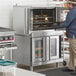 A man standing in front of a Main Street Equipment double deck convection oven with open doors.