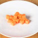 A plate of diced carrots with a Robot Coupe 3/8" x 3/8" Diced Carrots Kit on a wooden table.