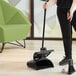 A person using a Lavex dustpan with a black handle to sweep a wood floor.