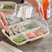 A hand holding a clear World Centric compostable container with 5 compartments of food inside.