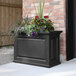 A black Mayne Nantucket rectangular planter with purple flowers on an outdoor patio table.