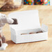 A hand holding a piece of chocolate candy in a white candy box.
