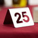 A Tablecraft stainless steel number 25 table tent on a table with a red tablecloth.