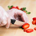 A person in gloves uses a Mercer Millennia paring knife to cut a strawberry.