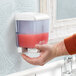 A hand holding a San Jamar blue liquid soap dispenser and pressing soap into it.