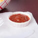A Solo white paper portion cup filled with red sauce on a white surface.