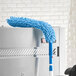 A Lavex 24" Flex Wand Duster with a blue chenille sleeve attached to a metal wall.