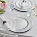 A white table set with 13" silver beaded rim charger plates, glasses, and flowers.