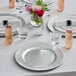 A table set with Choice silver beaded plastic charger plates, glasses, and flowers.