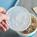 A hand using a Dart translucent plastic lid with a straw slot on a cup of ice