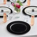A table set with Choice black plastic charger plates, glasses, and flowers.
