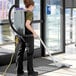 A woman using a ProTeam backpack vacuum to clean a carpet in a store aisle.