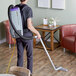 A man using a ProTeam backpack vacuum to clean a wood floor.