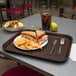 A Carlisle chocolate brown plastic fast food tray with a sandwich, chips, and a drink on it.