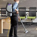 A person wearing a ProTeam backpack vacuum cleaning a carpeted floor.