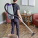 A man using a ProTeam backpack vacuum to clean a room.