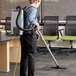 A woman wearing a backpack vacuuming the floor in a corporate office cafeteria with a ProTeam vacuum.