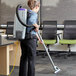 A woman using a ProTeam backpack vacuum to clean an office cafeteria floor.