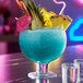 A blue cocktail fish bowl with fruit and straws in it.
