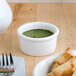 A white Tuxton china ramekin filled with green sauce on a plate with food and a fork.