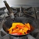 A Vollrath French style carbon steel fry pan full of sautéed yellow and orange peppers on a stove.