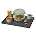 A black Cambro non-skid tray with a plate of food and a bowl of soup on a table.