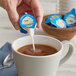 A person pouring International Delight French Vanilla non-dairy creamer into a cup of coffee.