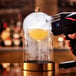 A person using a Flavour Blaster to make a glass of liquid under a large glass cloche.