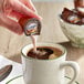 A person pouring International Delight HERSHEY'S Chocolate Caramel creamer into a cup of coffee.