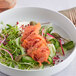 A close up of a bowl of salad with salmon, cucumbers, and vegetables.