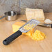 A Tablecraft stainless steel fine grater with a black handle grating cheese on a cutting board.