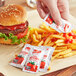 A hand putting French's Tomato Ketchup on a hamburger and fries using a small packet.