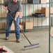 A man using a Lavex push broom with a black metal handle to sweep the floor.