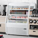 An Avantco white vertical air curtain merchandiser with various drinks and beverages inside.