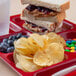 A red tray with a sandwich, potato chips, and blueberries.